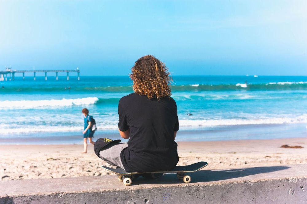 man sitting on skateboard looking at waves